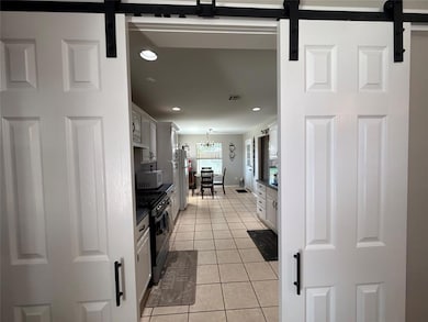 Kitchen featuring white appliances, a barn door, light tile patterned flooring, recessed lighting, and white cabinetry