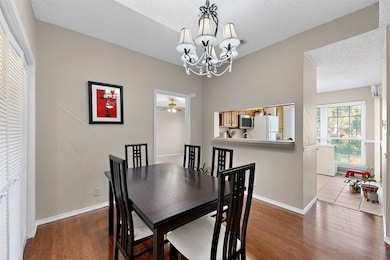 Dining space featuring a textured ceiling, wood-style floors, a chandelier & a ceiling fan. Add stools to create more seating around the barl. This layout provides an open floor plan.