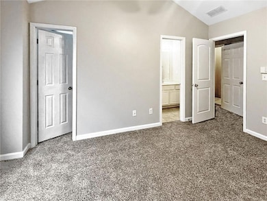 Unfurnished bedroom featuring carpet floors, baseboards, ensuite bath, and vaulted ceiling