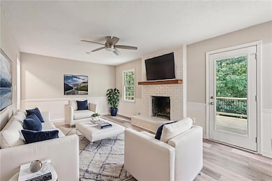 Living area with a wainscoted wall, light wood-style flooring, a ceiling fan, and a fireplace