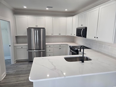 Kitchen featuring freestanding refrigerator, a sink, white cabinetry, crown molding, and tasteful backsplash