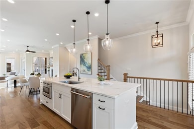 Kitchen featuring stainless steel dishwasher, ceiling fan, crown molding, open floor plan, and wood finished floors