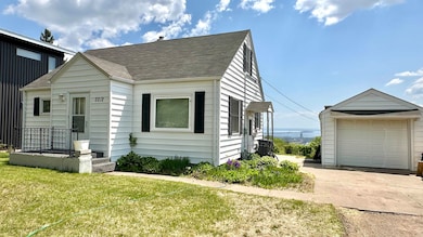 View of front facade with driveway, a front yard, a shingled roof, and a detached garage
