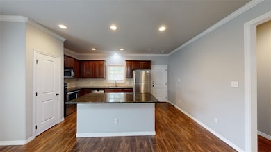 Kitchen featuring decorative backsplash, dark stone counters, crown molding, dark wood-style floors, and stainless steel appliances