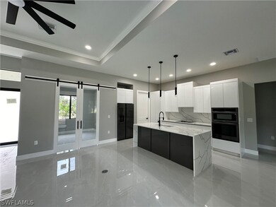 Kitchen with a barn door, ceiling fan, white cabinets, and a kitchen island with sink