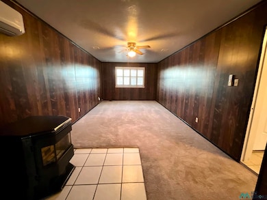 Spare room featuring light carpet, light tile patterned floors, wood walls, a wall unit AC, and a wood stove