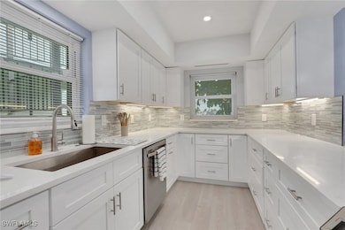 Kitchen featuring decorative backsplash, white cabinetry, light stone counters, and light wood-style floors