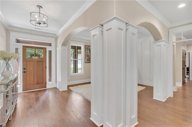 Entrance foyer with arched walkways, crown molding, light wood-type flooring, and a chandelier