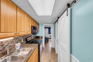 Kitchen featuring electric stove, black microwave, a barn door, decorative backsplash, and light tile patterned floors