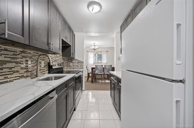 Kitchen featuring appliances with stainless steel finishes, backsplash, a chandelier, and light stone counters