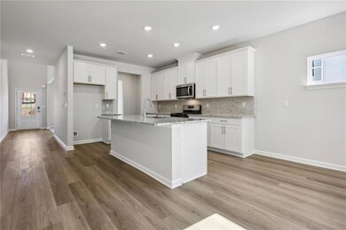 Kitchen with stainless steel appliances, white cabinets, decorative backsplash, light stone counters, and light wood-style flooring