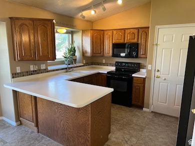Kitchen with brown cabinetry, black appliances, a peninsula, light countertops, and vaulted ceiling