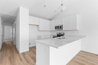 Kitchen featuring white cabinets, a peninsula, stainless steel appliances, light wood-style flooring, and light stone counters