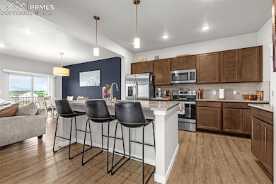 Kitchen with tasteful backsplash, appliances with stainless steel finishes, a kitchen breakfast bar, light countertops, and light wood finished floors