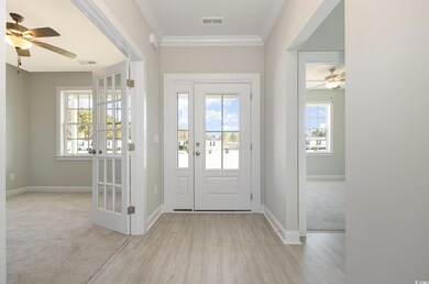 Carpeted entryway featuring ceiling fan and ornamental molding