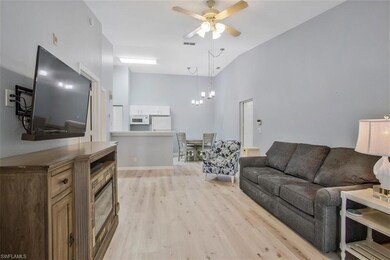 Living room with high vaulted ceiling, light wood-type flooring, and ceiling fan with notable chandelier