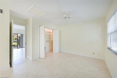 Unfurnished bedroom with attic access, light tile patterned flooring, a walk in closet, a ceiling fan, and a closet