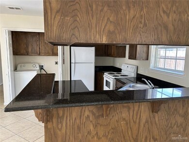 Kitchen featuring white appliances, washer / dryer, light tile patterned floors, dark stone counters, and a sink