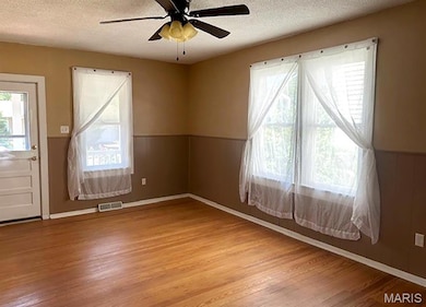 Empty room with a ceiling fan, light wood finished floors, and a textured ceiling
