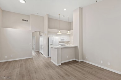 Kitchen with a high ceiling, arched walkways, white cabinets, a peninsula, and light wood finished floors