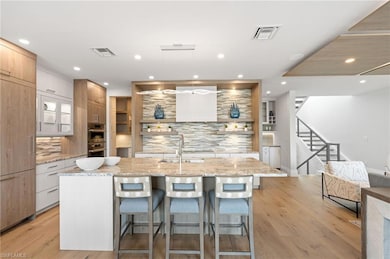 Kitchen with double oven, a sink, a kitchen breakfast bar, modern cabinets, and backsplash