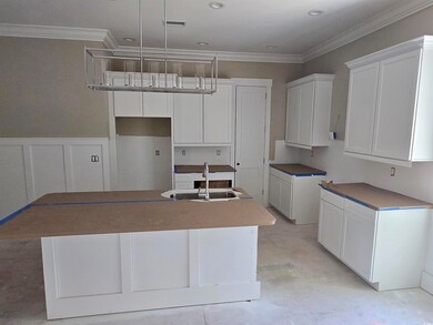 Kitchen with visible vents, a center island with sink, unfinished concrete flooring, a sink, and white cabinetry