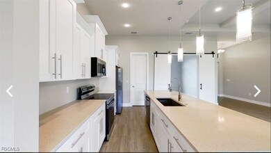 Kitchen featuring a barn door, white cabinets, appliances with stainless steel finishes, pendant lighting, and dark wood-style flooring