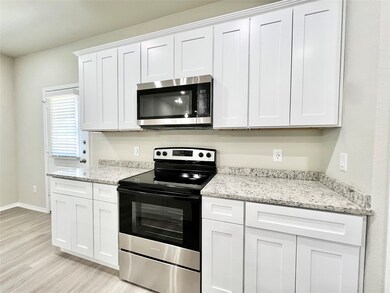 Kitchen featuring stainless steel appliances, white cabinetry, light stone countertops, and light wood finished floors