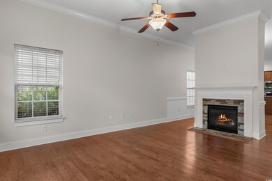 Unfurnished living room featuring crown molding, dark wood-style flooring, a fireplace with flush hearth, and a ceiling fan