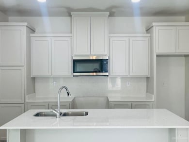 Kitchen with backsplash, stainless steel microwave, light stone counters, and white cabinetry