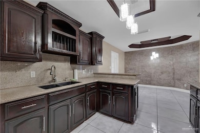 Kitchen with dark brown cabinetry, a notable chandelier, a sink, light countertops, and a peninsula