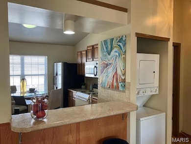 Kitchen featuring electric range, tasteful backsplash, light countertops, stainless steel microwave, and lofted ceiling