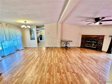  ceiling fan with notable chandelier, light hardwood / wood-style floors, a textured ceiling, and a stone fireplace