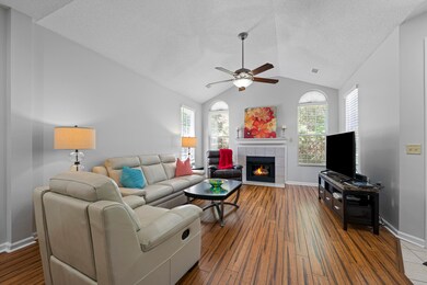 Living room with a ceiling fan, a fireplace, vaulted ceiling, healthy amount of natural light, and dark wood-style flooring