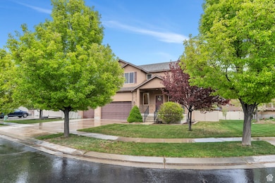 View of property hidden behind natural elements featuring fence, a front lawn, concrete driveway, an attached garage, and stucco siding