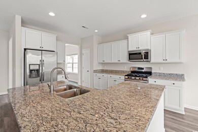 Kitchen with stainless steel appliances, a sink, white cabinets, a center island with sink, and light wood-type flooring