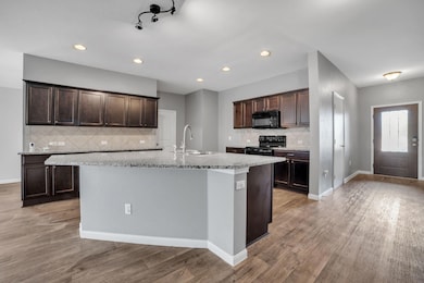 Kitchen featuring dark brown cabinetry, decorative backsplash, light stone counters, black appliances, and recessed lighting