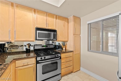 Kitchen featuring light brown cabinets, stainless steel appliances, dark stone countertops, and light tile patterned floors