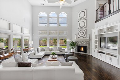 This living room is more like a GREAT room featuring a stunning fireplace with mantel detailing, custom paint, soaring high ceiling, recessed lighting, light stained ceiling fan with lighting, wood flooring, and an amazing wall of windows providing a lovely view of your backyard to keep an eye out on the kids or pets playing.