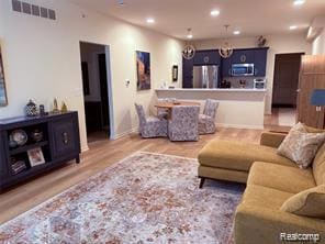 Living room with recessed lighting, light wood-style flooring, and a chandelier