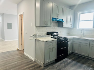 Kitchen featuring black gas range oven, dark wood-style floors, backsplash, under cabinet range hood, and light stone countertops