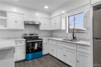 Kitchen featuring wood tiled floor, range hood, range with electric stovetop, white cabinetry, and a sink