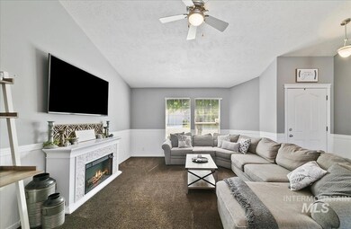 Living room with ceiling fan, a wainscoted wall, a textured ceiling, dark colored carpet, and a glass covered fireplace