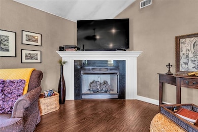 Living area featuring wood finished floors, a fireplace, vaulted ceiling, and baseboards