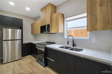 Kitchen featuring stainless steel appliances, modern cabinets, light wood finished floors, dark cabinets, and light stone counters