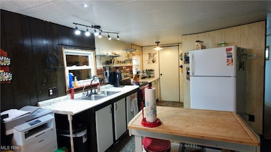 Kitchen with light countertops, freestanding refrigerator, dark cabinets, stainless steel range with electric cooktop, and wood walls