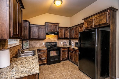 Kitchen with black appliances, dark brown cabinets, under cabinet range hood, vaulted ceiling, and tasteful backsplash