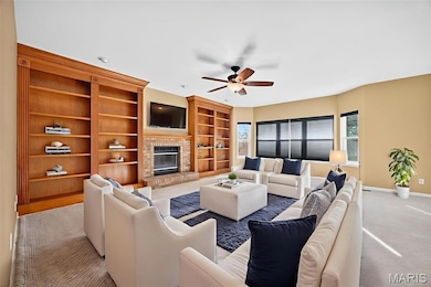 Carpeted living area featuring built in shelves, a brick fireplace, and ceiling fan