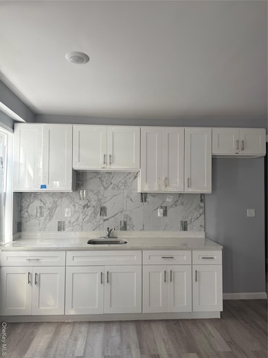 Kitchen with white cabinets, backsplash, light wood-style flooring, and light stone counters