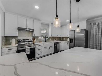 Kitchen with hanging light fixtures, appliances with stainless steel finishes, white cabinets, farmhouse sink, and tasteful backsplash
